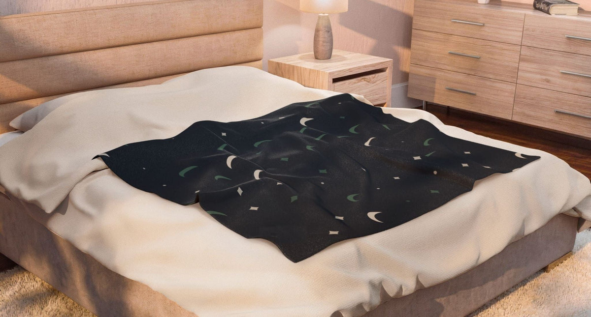 A dim, calm bedroom with a bedside lamp and the Cove starry throw on the bed