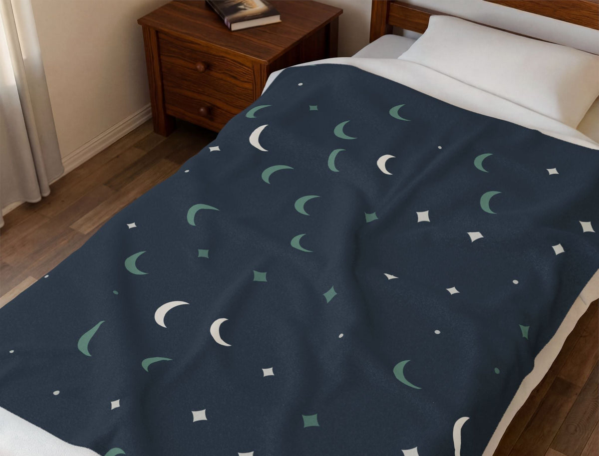 Navy moon-and-stars Cove throw on a made bed beside a wooden nightstand